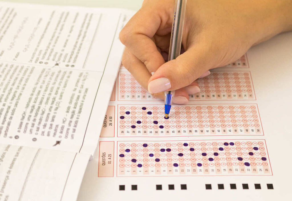 estudante preenchendo gabarito de prova representando a escolha entre vestibular ou Enem