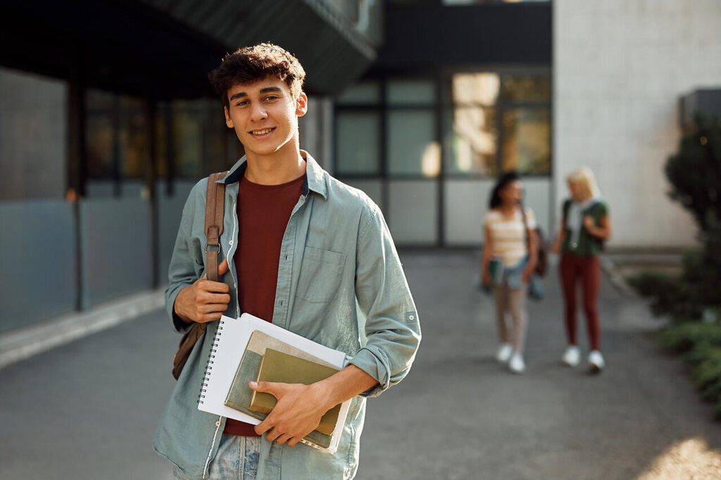 Estudante segurando livros em frente à faculdade, representando a preparação focada nos assuntos de biologia que mais caem no Enem.