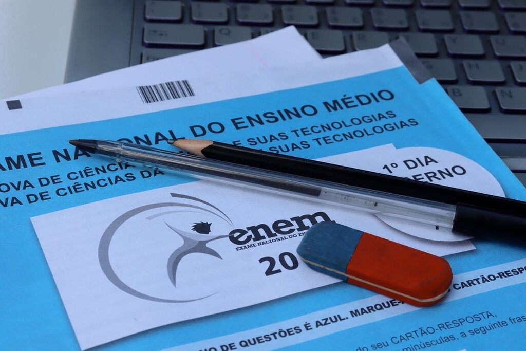 Close em caderno de questões do ENEM 2026 com caneta preta, lápis e borracha sobre a mesa.